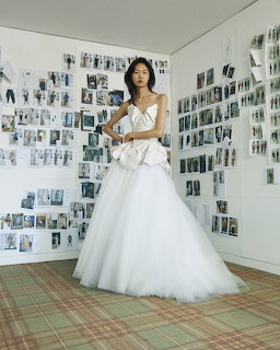 Model in white bridal gown with tulle skirt standing in front of walls covered in pined fashion photos