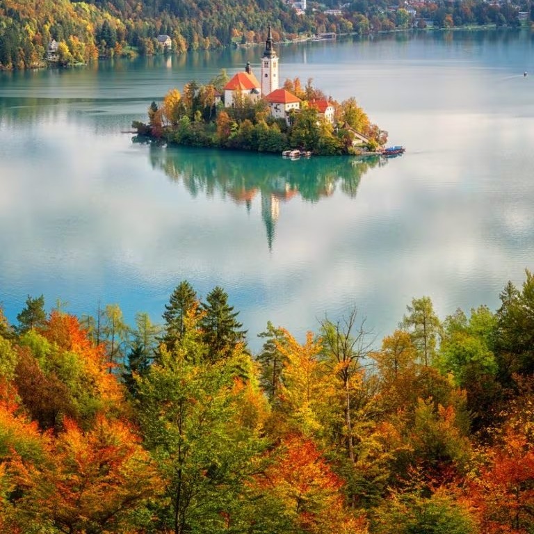 Church on island in turquoise lake surrounded by autumn trees and mountains