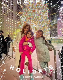 Woman and two girls smiling in front of lit Christmas tree at night