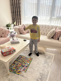 Young boy in yellow shirt standing in living room next to a colorful completed puzzle on the floor