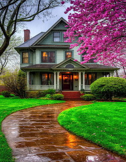 Victorian house with lit porch and pink flowering tree on a rainy spring evening