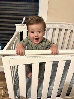 Smiling baby standing in a white crib indoors