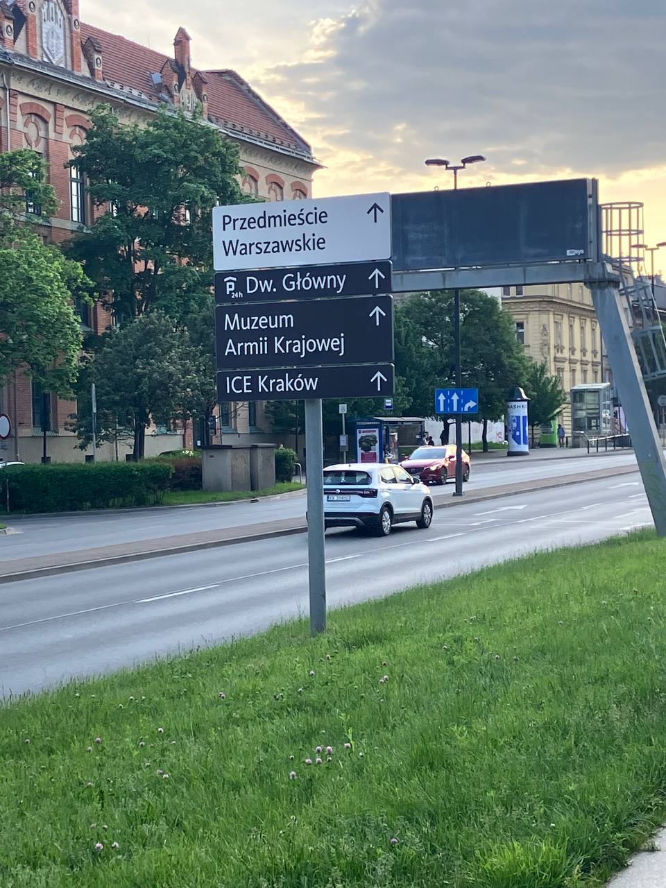 Directional street signs near a road with a parked car and old buildings in a Polish city