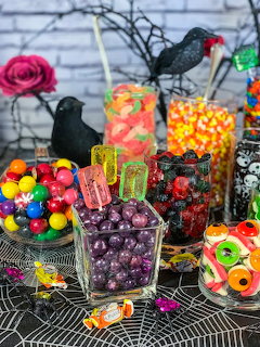 Halloween candy bar with glass jars of colorful candies, black crow decorations, and spiderweb tablecloth
