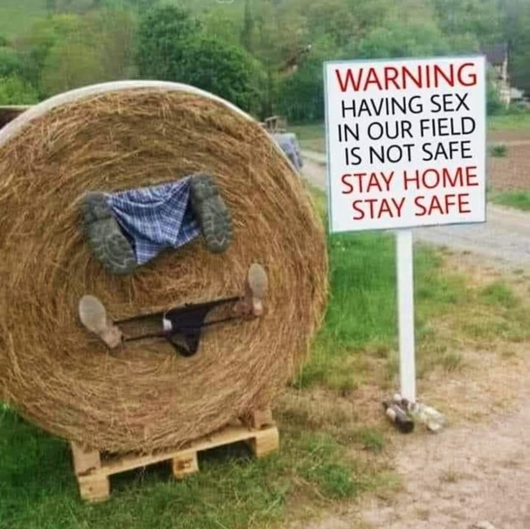 Warning sign next to large hay bale on wooden pallet in rural field setting