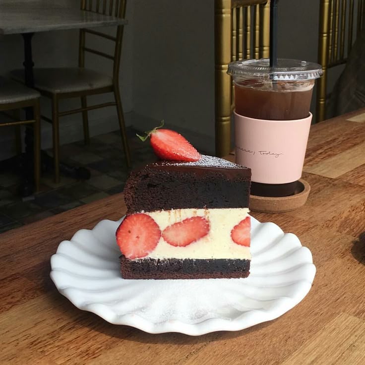 Chocolate layer cake slice with strawberries and cream next to iced coffee on wooden cafe table
