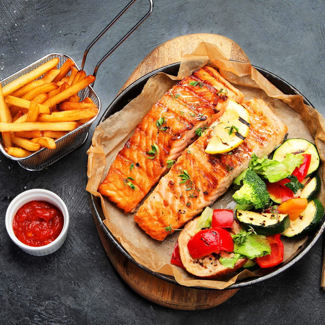 Grilled salmon fillet with french fries, fresh salad and cherry tomatoes on wooden board