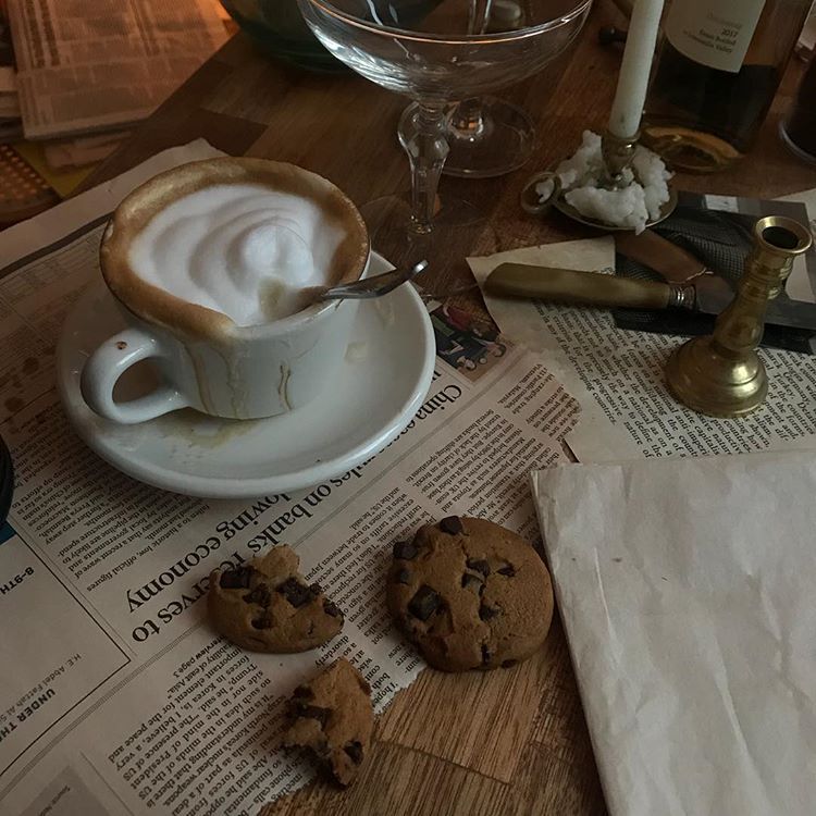 Cappuccino with foam art and chocolate chip cookies on a newspaper-covered table