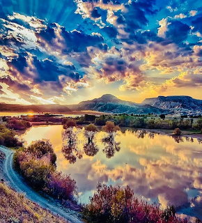 Colorful sunset reflecting in calm lake with mountains and dramatic clouds in orange, pink, and blue sky