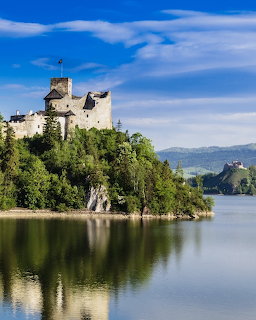 Medieval castle on forested hill above tranquil lake with blue sky