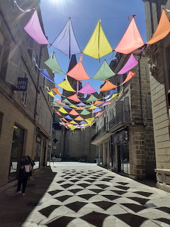 Colorful geometric fabric canopies hanging over a narrow stone street with black and white checkered ground