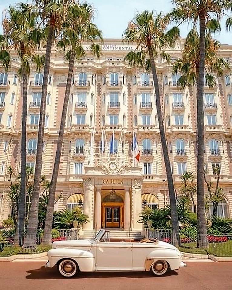 Grand Carlton Hotel building in Cannes with palm trees and classic white car in front