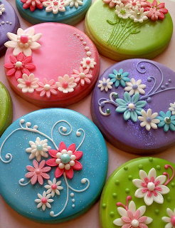 Round cookies decorated with colorful icing flowers in pink, purple, green, and blue with white floral details