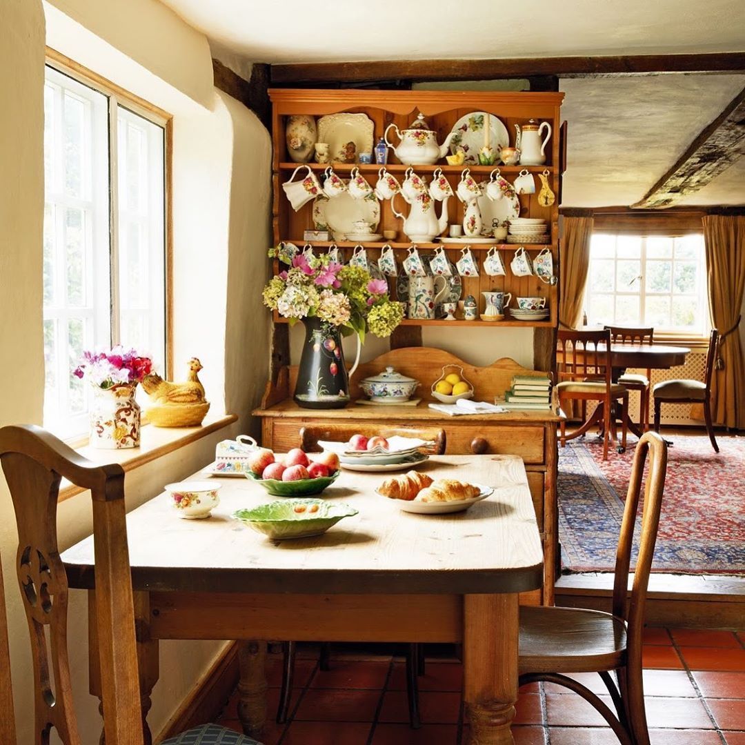 Rustic cottage kitchen with wooden table, antique hutch, pottery display, and sunny windows