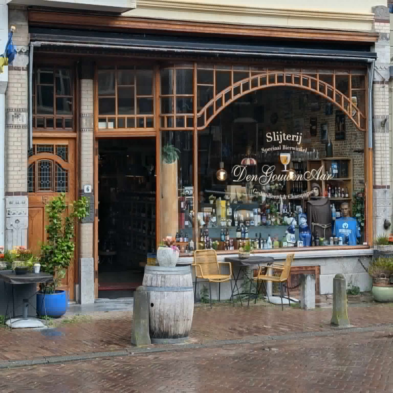 Traditional shopfront with arched windows, wooden trim, and outdoor chairs on a wet street