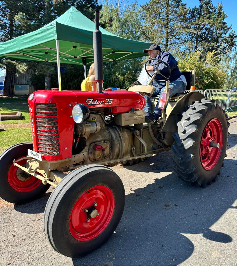 Man riding a vintage red Zetor 25 tractor at an outdoor event with a green tent in the background
