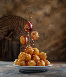 Stack of golden fried pastry balls drizzled with honey on white plate
