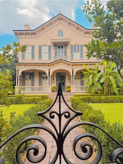 Decorative iron gate in front of a peach-colored Victorian mansion with white trim and lush garden
