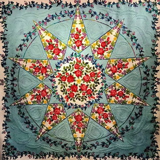 Eight-pointed star quilt with floral fabrics in red, cream, and teal on patterned background