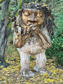 Wooden troll sculpture with mossy hair holding bird, made from recycled wood in forest