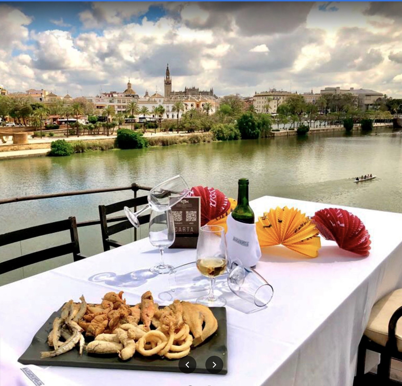 Riverside restaurant table with fried seafood, wine bottle, glasses, and a city view across the water.