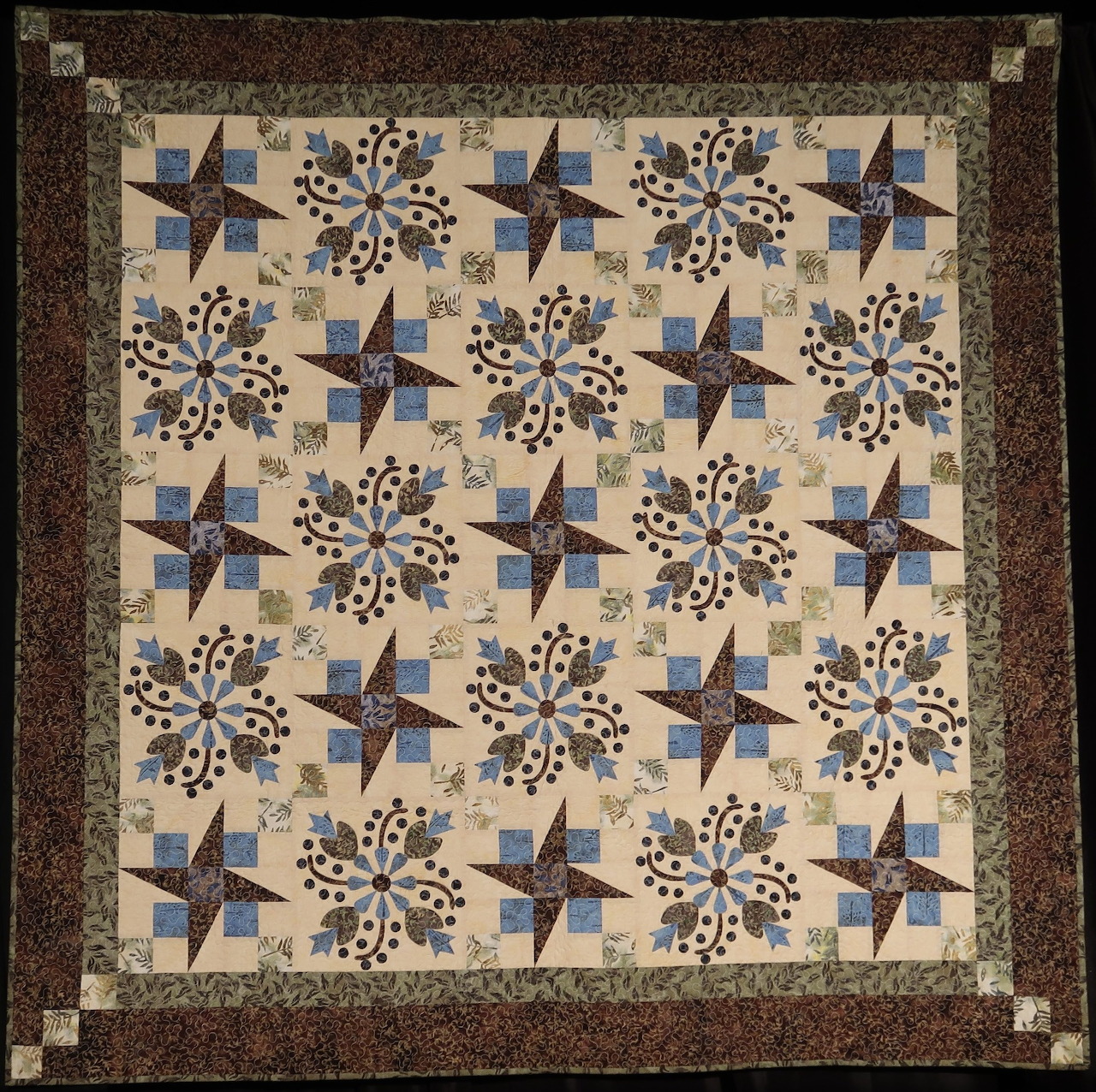 Quilt with blue star blocks and brown floral motifs arranged in a grid pattern with ornate borders